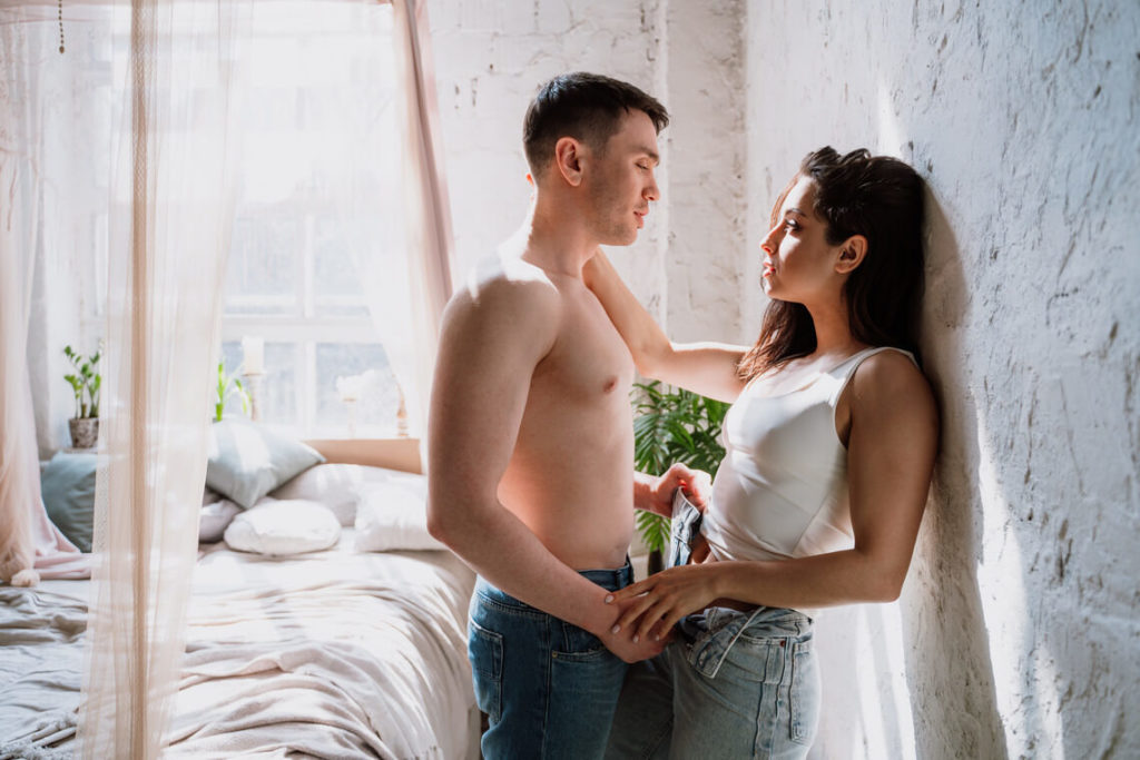 young couples from denver are intimately staring one another while standing near a bed as the guy is topless